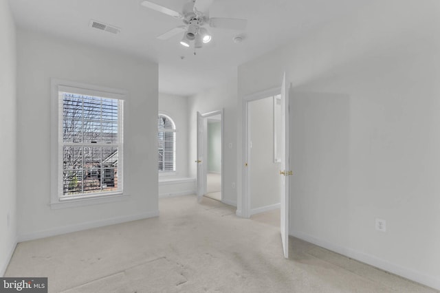 carpeted empty room featuring visible vents, a ceiling fan, and baseboards