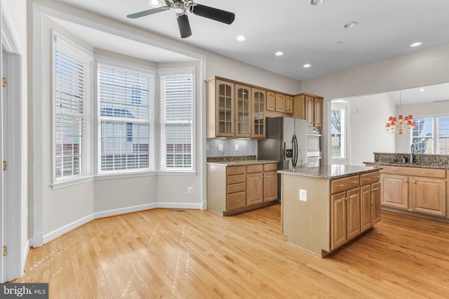 kitchen featuring a kitchen island, a sink, glass insert cabinets, light wood-type flooring, and backsplash