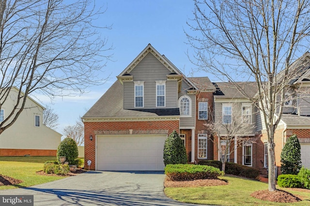 traditional-style home featuring brick siding, aphalt driveway, a front yard, and roof with shingles