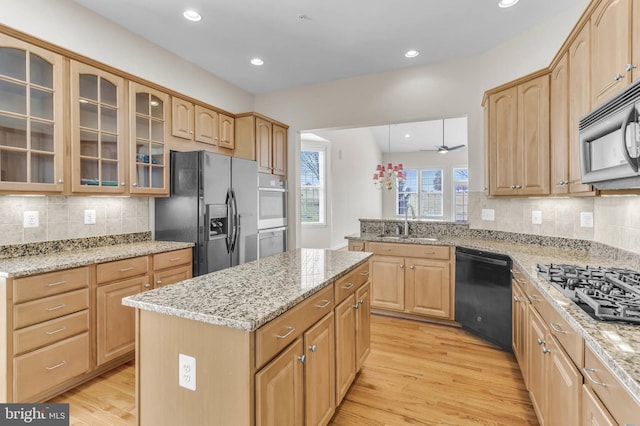 kitchen with black appliances, glass insert cabinets, light wood-style floors, and a sink