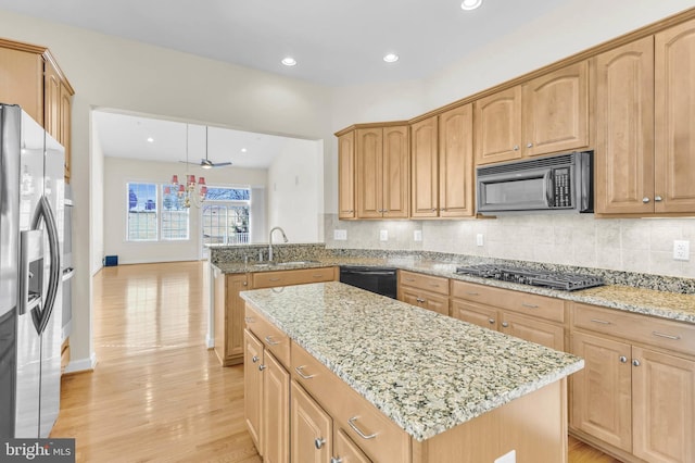 kitchen with a kitchen island, light wood-type flooring, light stone counters, black appliances, and a sink