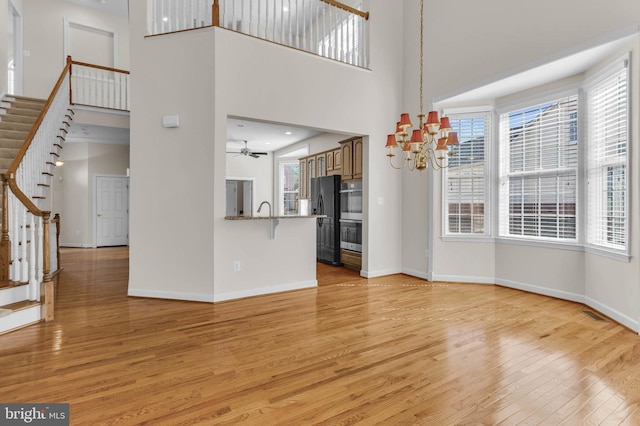 unfurnished living room featuring stairs, light wood-style floors, baseboards, and a wealth of natural light