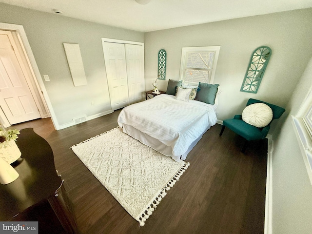 bedroom with baseboards, visible vents, dark wood finished floors, and a closet