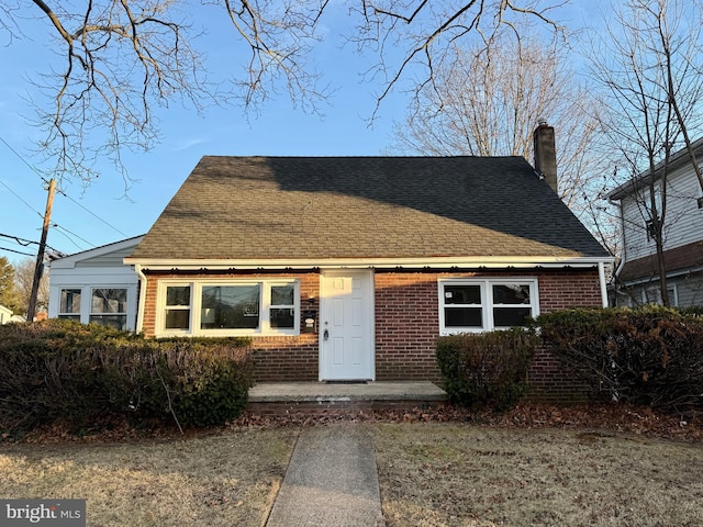 view of front of property featuring roof with shingles, a chimney, and brick siding