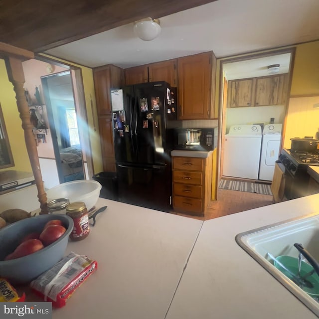kitchen with brown cabinets, light countertops, washer and dryer, black appliances, and a sink
