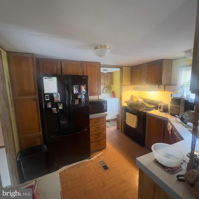 kitchen with light countertops, visible vents, brown cabinetry, washer / dryer, and black appliances