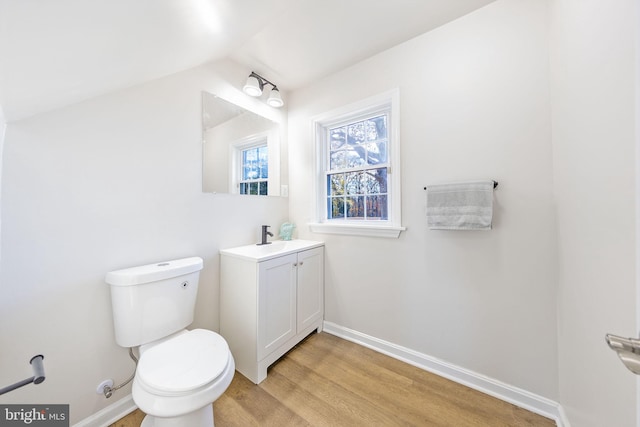 half bathroom with vanity, toilet, wood finished floors, and baseboards