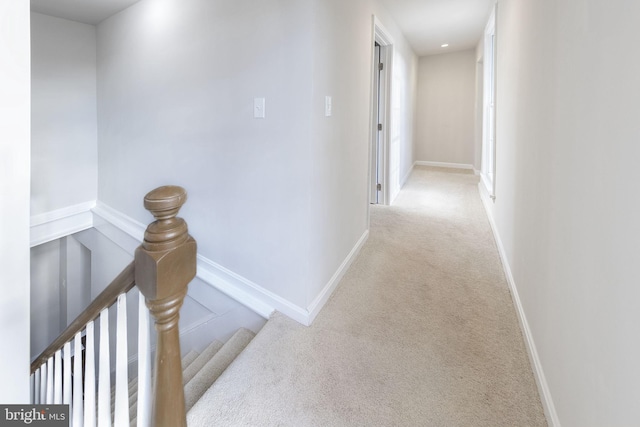 hall featuring baseboards, an upstairs landing, and light colored carpet