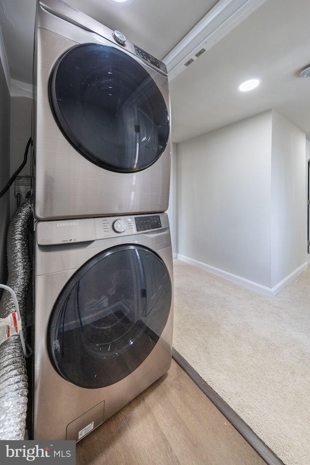 clothes washing area featuring baseboards, stacked washer / drying machine, laundry area, and light carpet