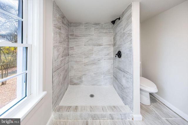 full bath featuring a tile shower, a healthy amount of sunlight, and toilet