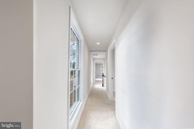 hallway with baseboards, visible vents, and light carpet