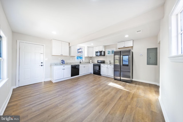 kitchen with light countertops, visible vents, white cabinets, black appliances, and electric panel