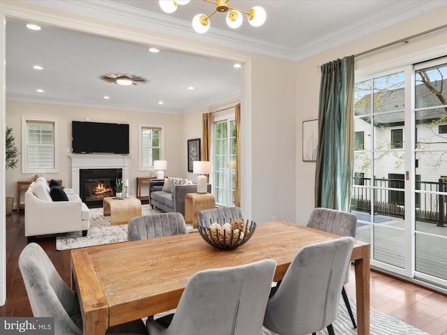 dining area featuring recessed lighting, an inviting chandelier, wood finished floors, crown molding, and a glass covered fireplace
