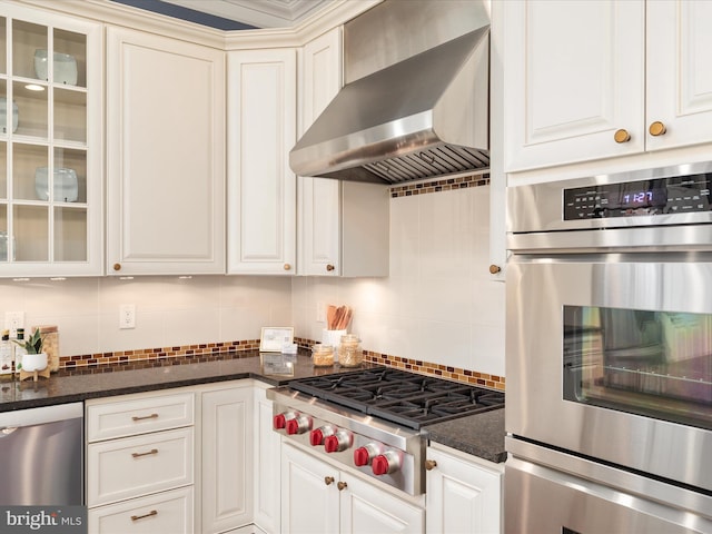 kitchen with stainless steel appliances, backsplash, glass insert cabinets, and wall chimney range hood