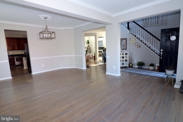 unfurnished living room featuring baseboards, dark wood-style floors, stairway, ornamental molding, and an inviting chandelier