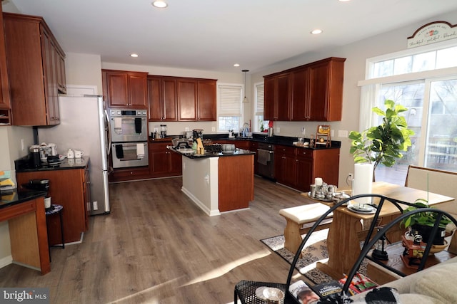 kitchen featuring a center island, dark countertops, appliances with stainless steel finishes, a sink, and wood finished floors