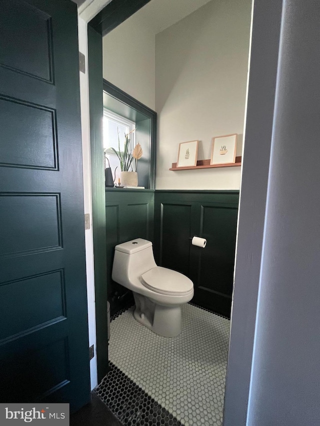 bathroom featuring tile patterned flooring, a wainscoted wall, a decorative wall, and toilet