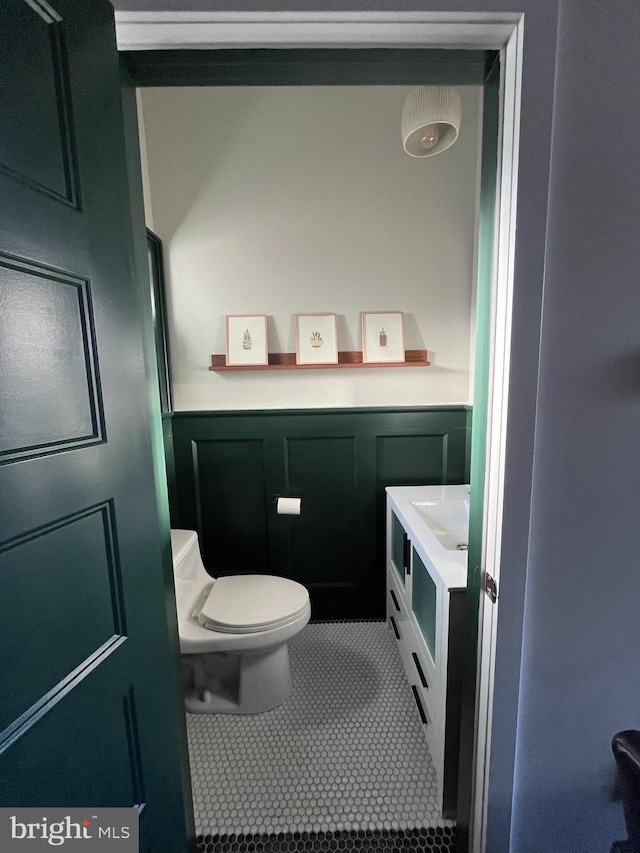 bathroom featuring wainscoting, toilet, tile patterned floors, vanity, and a decorative wall