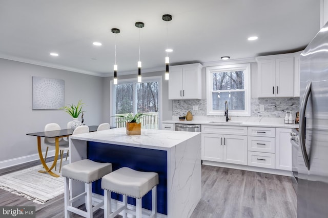 kitchen featuring light wood finished floors, ornamental molding, stainless steel appliances, and a sink