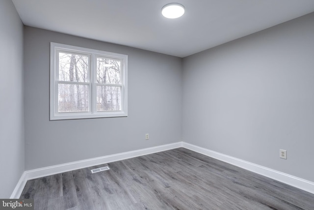 unfurnished room featuring wood finished floors, visible vents, and baseboards