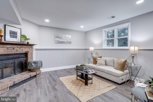 living area featuring a wainscoted wall, visible vents, a fireplace, and wood finished floors