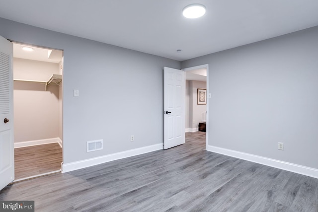 unfurnished bedroom featuring a spacious closet, wood finished floors, visible vents, and baseboards