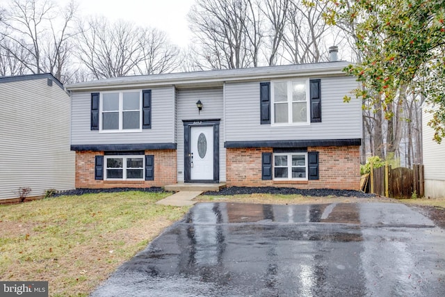 bi-level home featuring fence, a front lawn, and brick siding