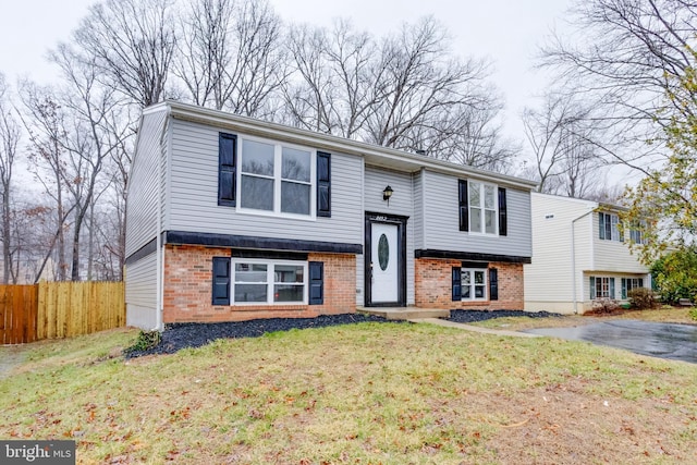 raised ranch featuring brick siding, a front yard, and fence