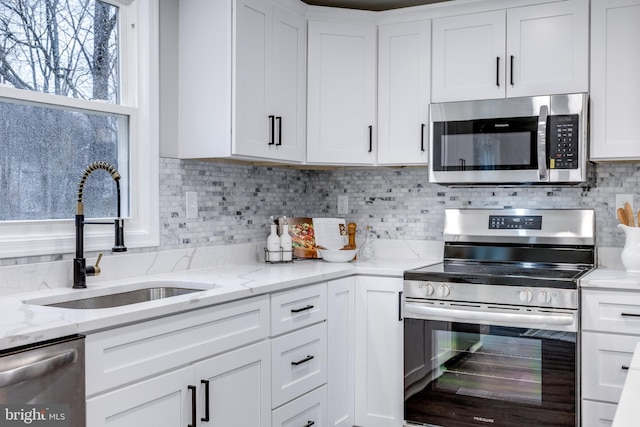 kitchen with stainless steel appliances, decorative backsplash, a sink, and white cabinets