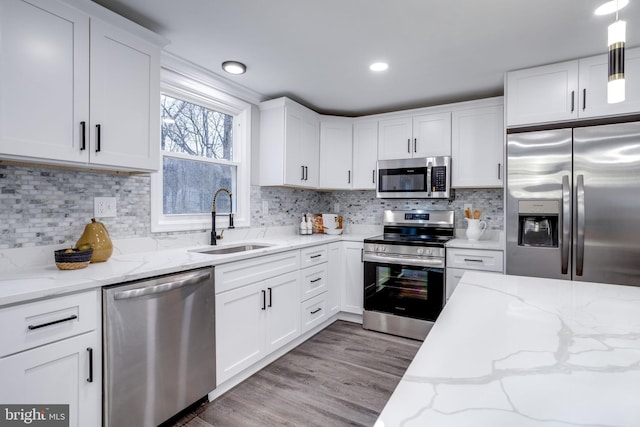 kitchen featuring stainless steel appliances, wood finished floors, a sink, white cabinets, and tasteful backsplash