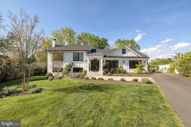 view of front facade with a chimney, aphalt driveway, board and batten siding, and a front yard