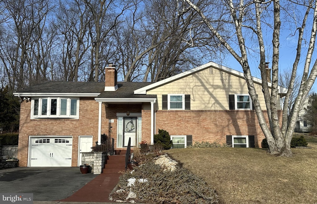 split foyer home with a garage, brick siding, a chimney, and aphalt driveway