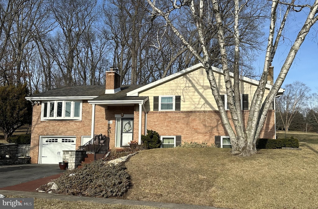 split foyer home with a garage, a chimney, aphalt driveway, a front lawn, and brick siding