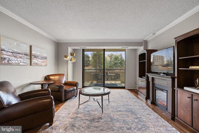 living area with a textured ceiling, ornamental molding, wood finished floors, and a glass covered fireplace