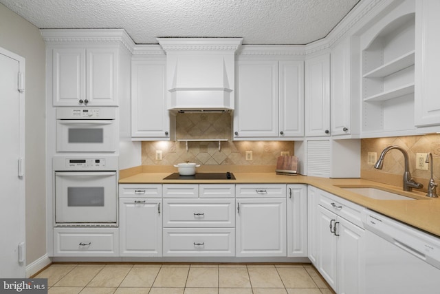 kitchen with white appliances, a sink, white cabinets, light countertops, and custom range hood