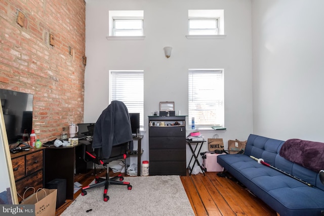 home office with brick wall, wood finished floors, and a towering ceiling