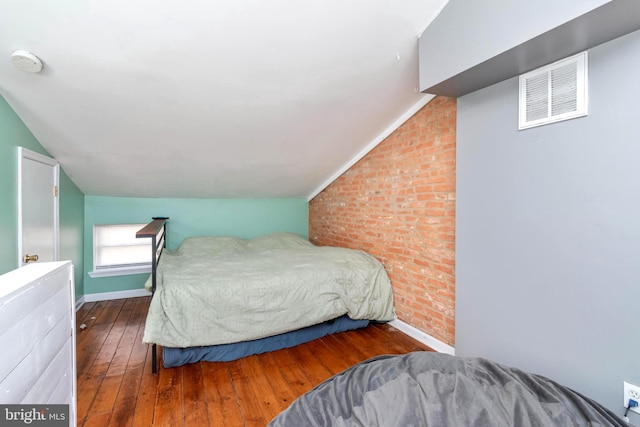 bedroom featuring baseboards, visible vents, lofted ceiling, brick wall, and wood finished floors