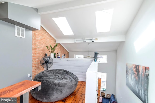 interior space featuring brick wall, lofted ceiling with skylight, wood finished floors, and visible vents