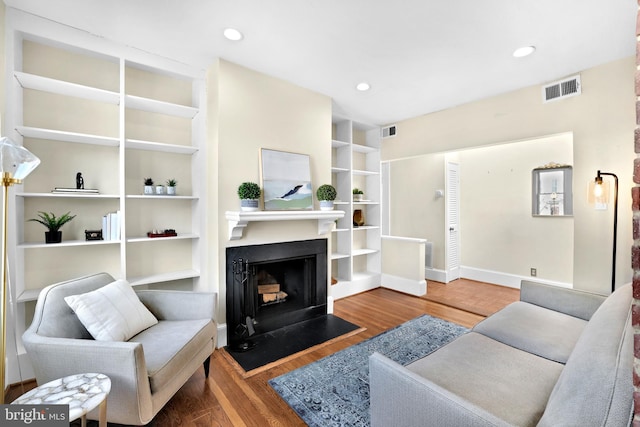 living room featuring a fireplace with flush hearth, wood finished floors, visible vents, and recessed lighting