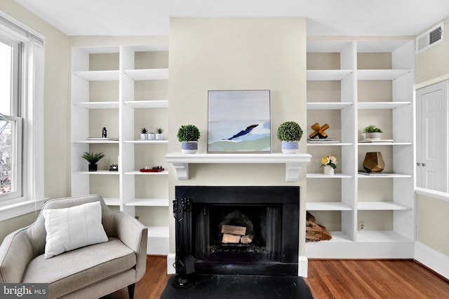 living area with a healthy amount of sunlight, a fireplace with flush hearth, visible vents, and wood finished floors