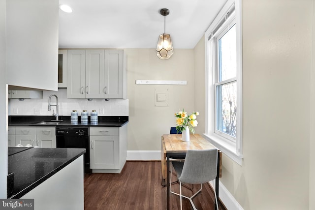 kitchen featuring dishwasher, dark countertops, a sink, and decorative light fixtures