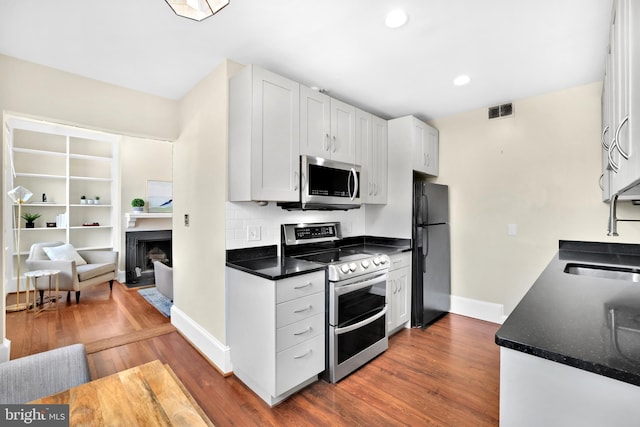 kitchen featuring visible vents, white cabinets, dark countertops, stainless steel appliances, and a sink