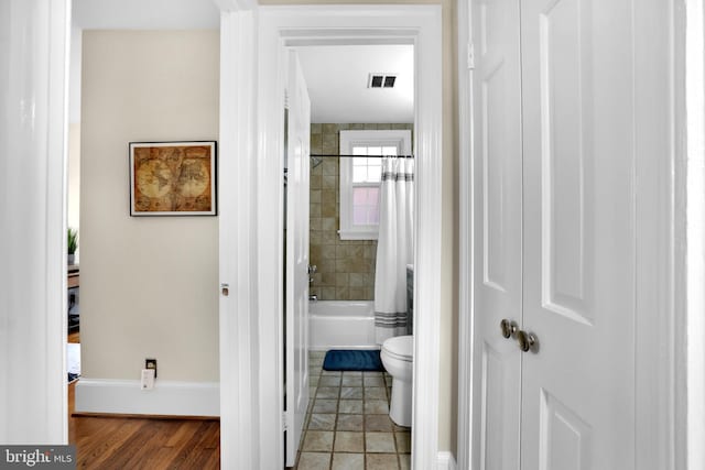 full bath featuring toilet, shower / bath combo with shower curtain, visible vents, and baseboards