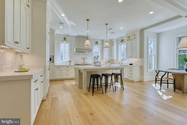 kitchen with white cabinets, light countertops, hanging light fixtures, a center island, and custom range hood