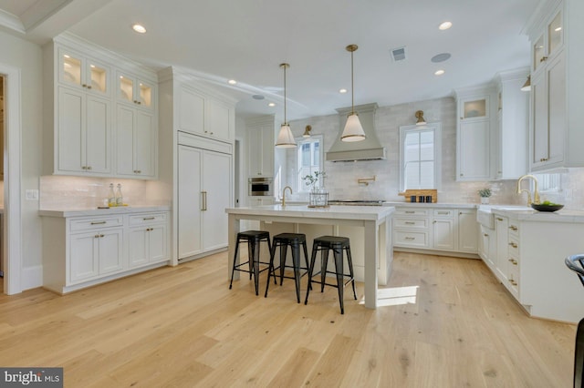 kitchen with light countertops, white cabinets, premium range hood, and an island with sink