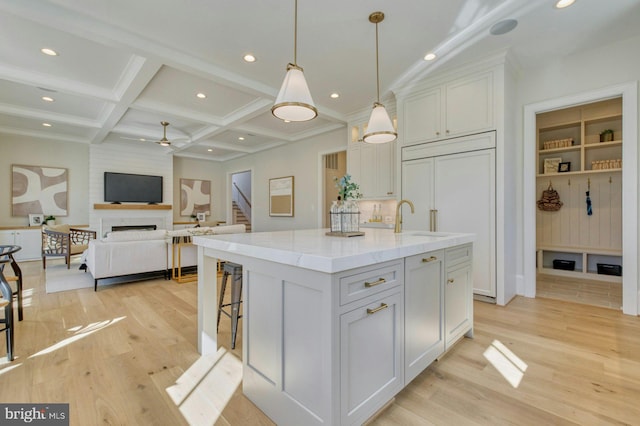 kitchen featuring pendant lighting, open floor plan, a kitchen island with sink, white cabinetry, and coffered ceiling