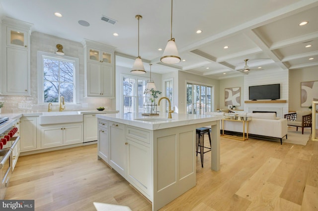 kitchen featuring white cabinets, open floor plan, an island with sink, glass insert cabinets, and pendant lighting