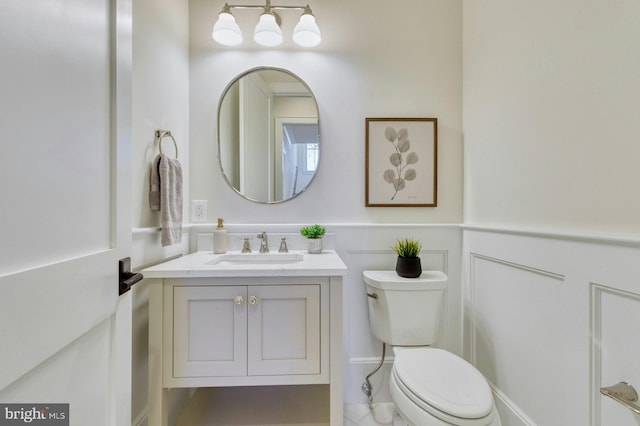 half bath featuring toilet, a wainscoted wall, a decorative wall, and vanity