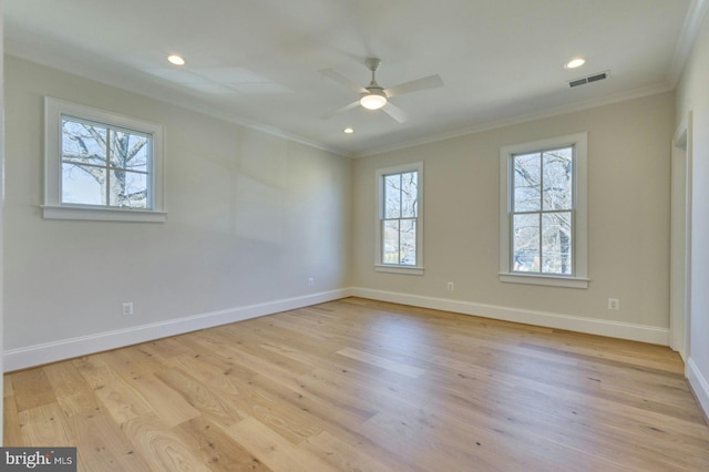 empty room featuring light wood-style floors, visible vents, crown molding, and baseboards