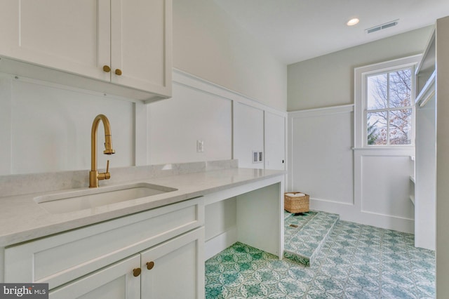 interior space with a decorative wall, a sink, visible vents, wainscoting, and light stone countertops